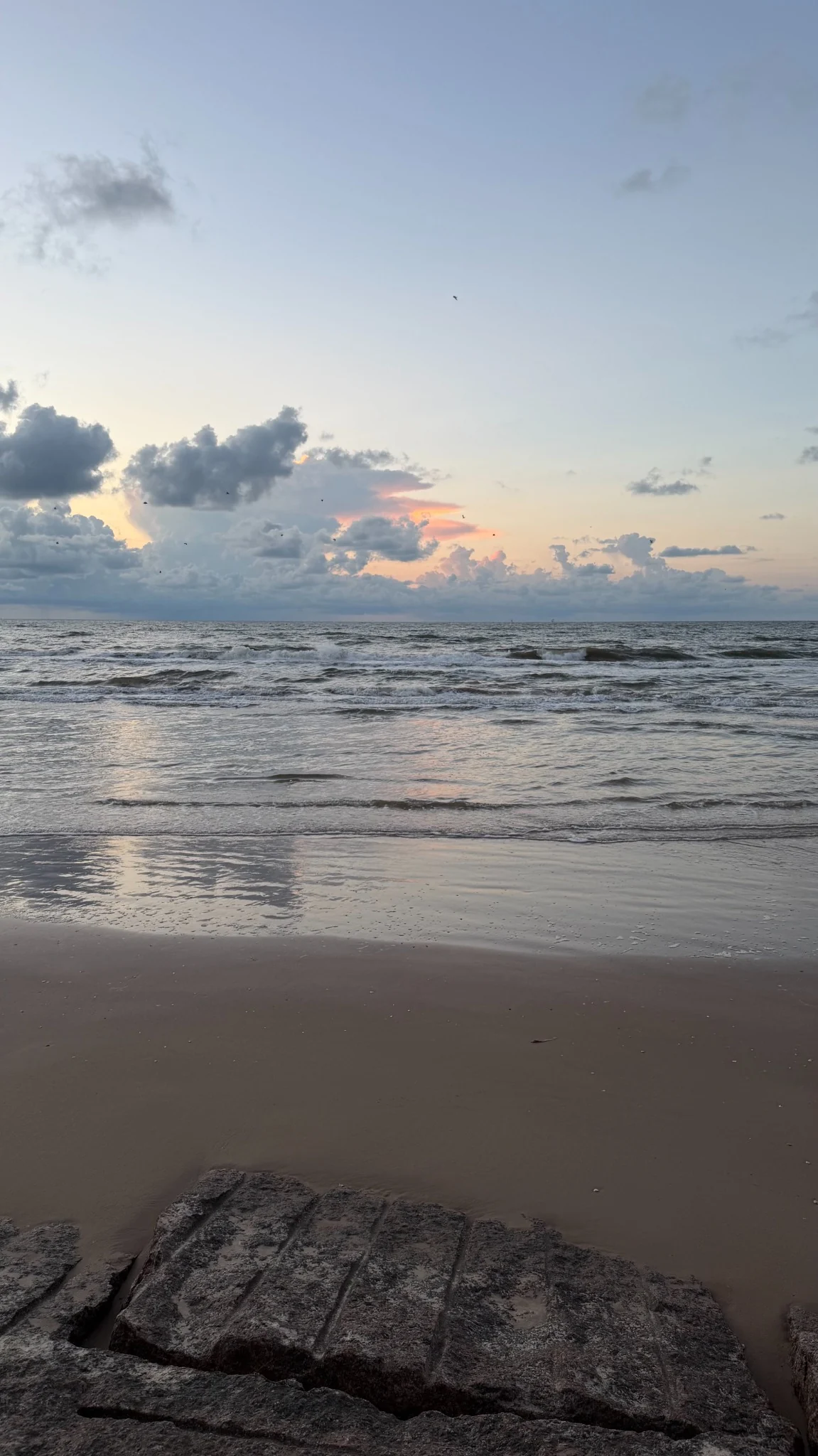 Brown-sand beach near the lodge with weathered limestone blocks and Gulf waves